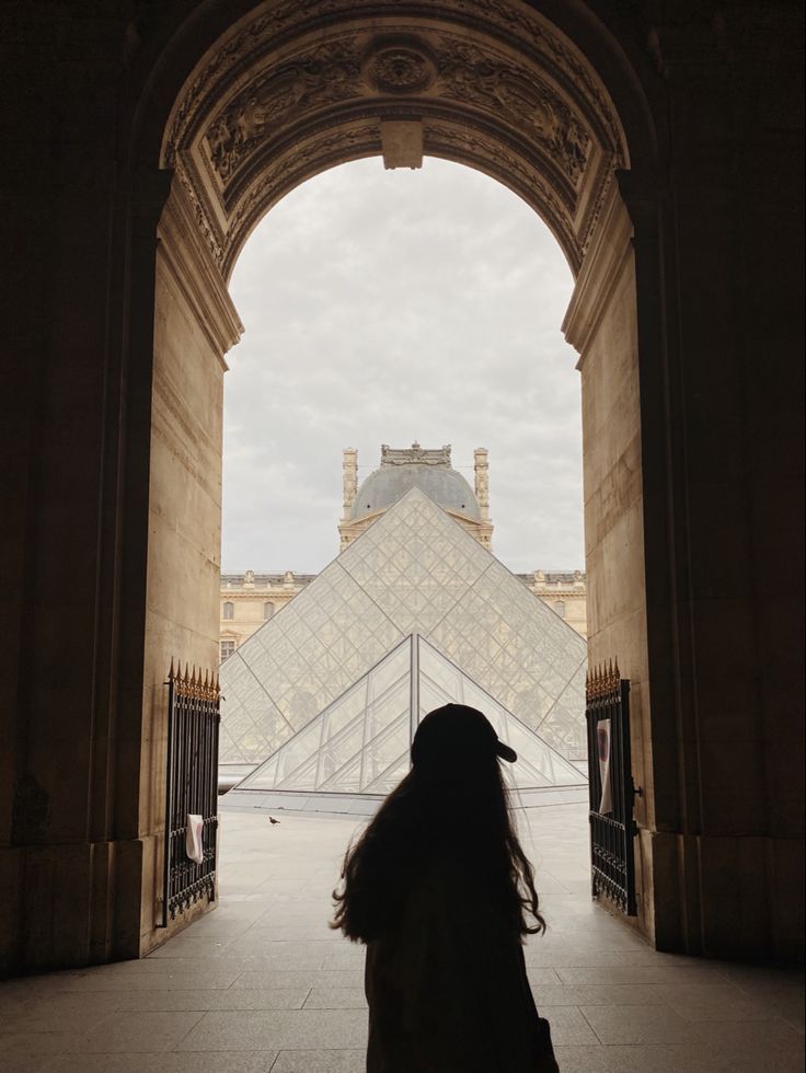 a woman standing in front of an entrance to a building with a glass pyramid behind her