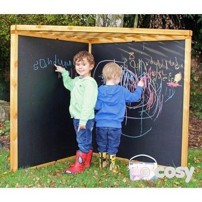 two young boys writing on a blackboard in front of a wooden structure with grass