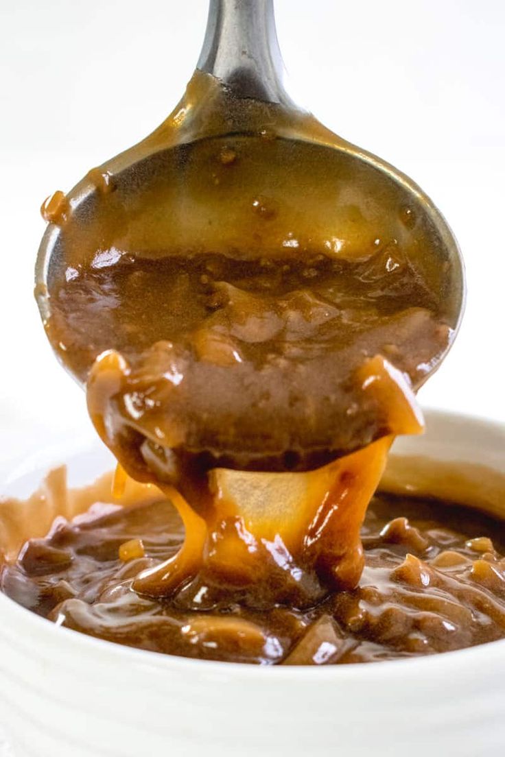 a spoon full of caramel sauce being lifted from a white bowl filled with food