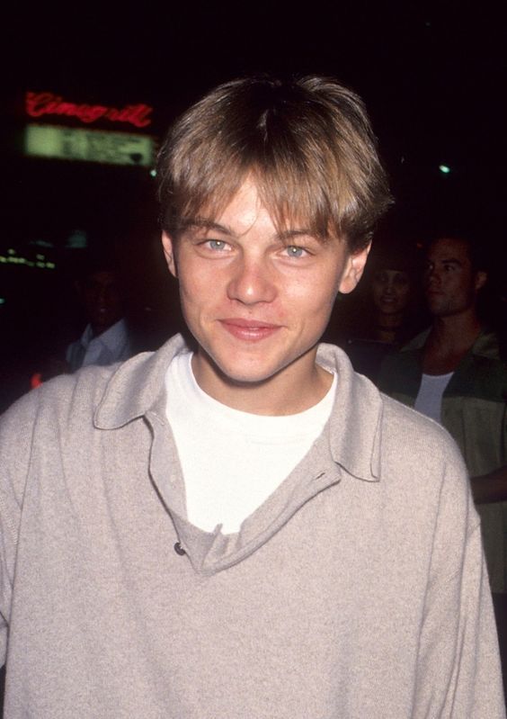 a young man standing in front of a crowd wearing a gray sweater and white shirt