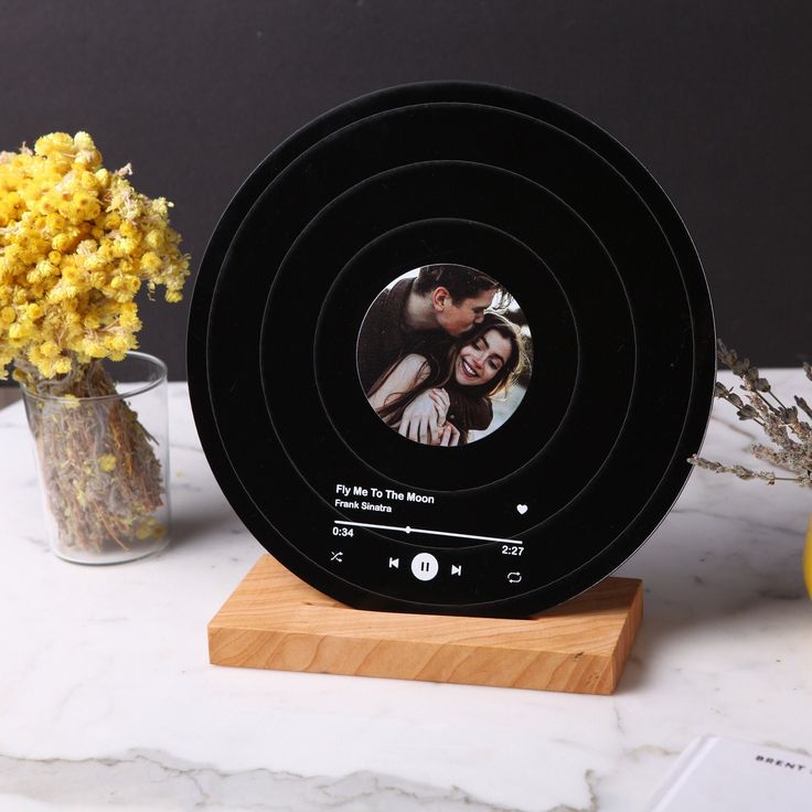 a black clock with a couple's photo on it and flowers in the background