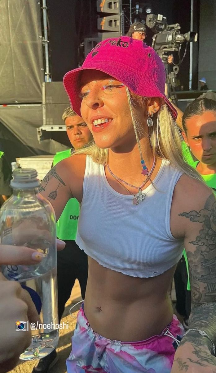 a woman wearing a pink hat and tank top holding a glass jar with liquid in it