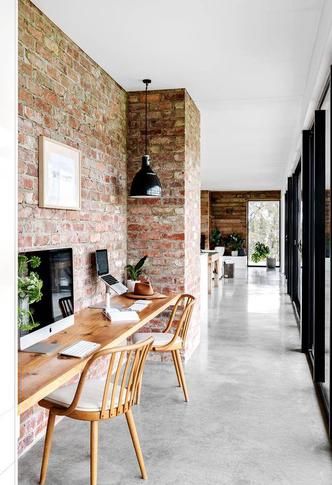 an empty room with brick walls and wooden chairs in front of a table that has a laptop on it