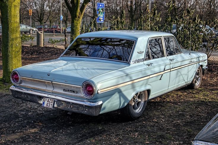 an old car is parked in the dirt near some trees and other things on the ground