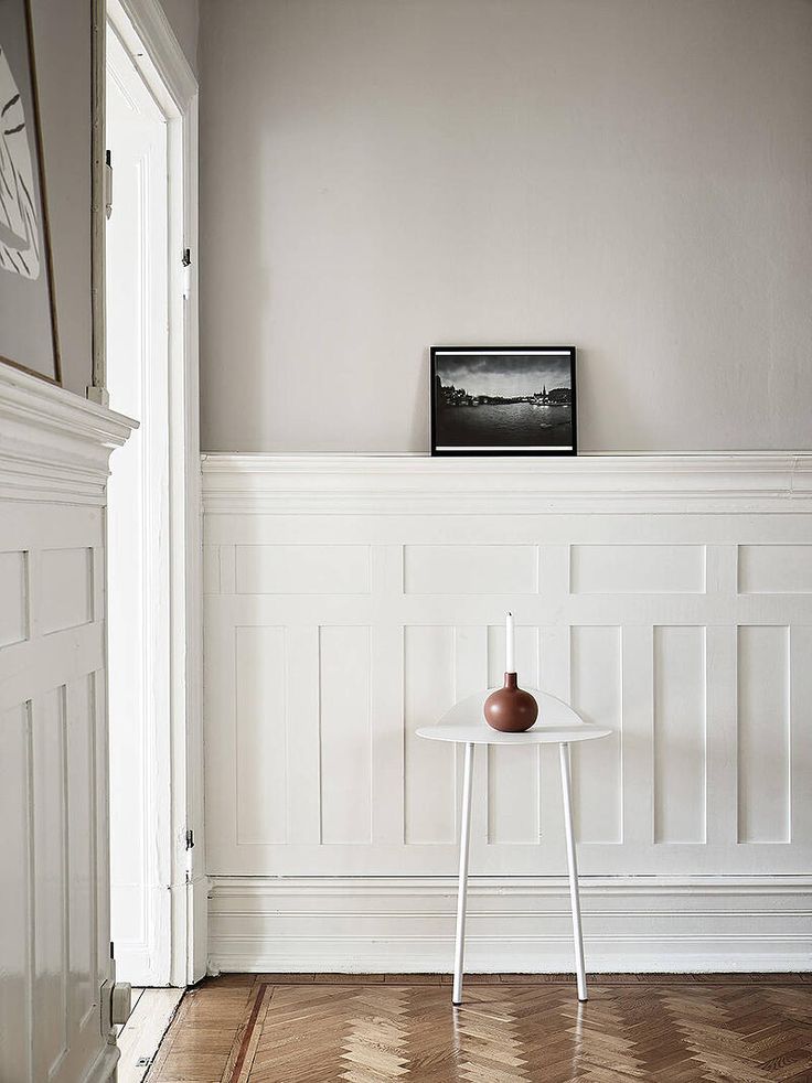 a table with a vase on it in front of a white wall and wooden floor