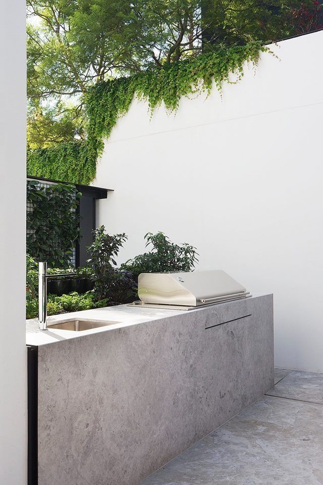 an outdoor kitchen with concrete counter tops and sink, surrounded by greenery on the wall