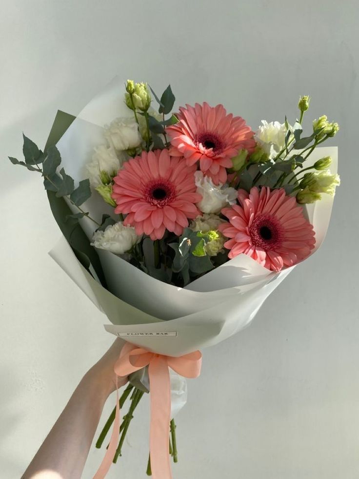 a person holding a bouquet of flowers with pink and white daisies on it's side