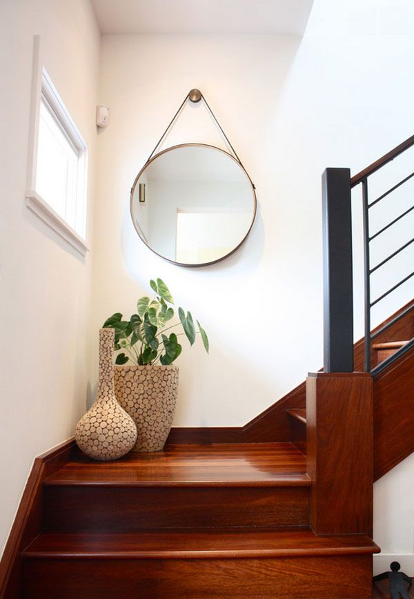 two vases with plants sit on the stairs next to a round mirror and metal railing