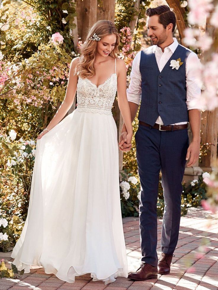 a bride and groom holding hands while walking down the path in front of some flowers