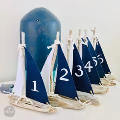 four sailboats are sitting on driftwood and tied to the pole with numbers painted on them