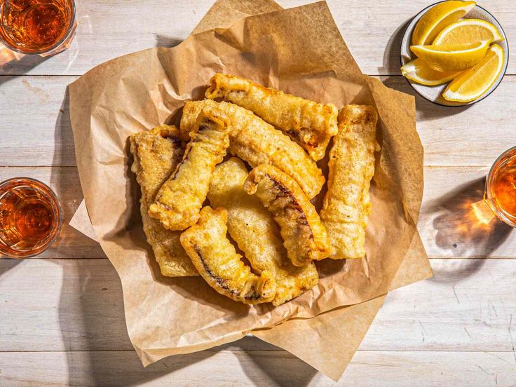 some fried food is sitting on top of a piece of paper next to glasses and lemon wedges