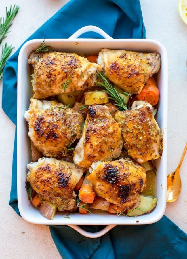 chicken and vegetables in a white casserole dish on a blue cloth with spoons