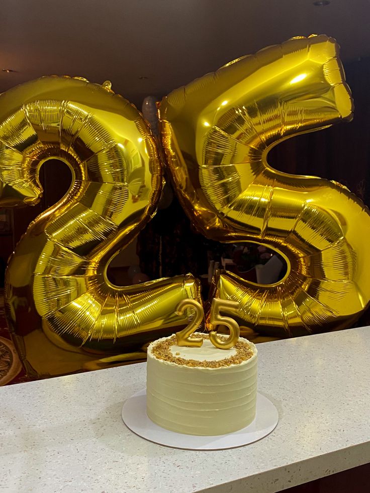 a white cake with gold balloons in the shape of numbers