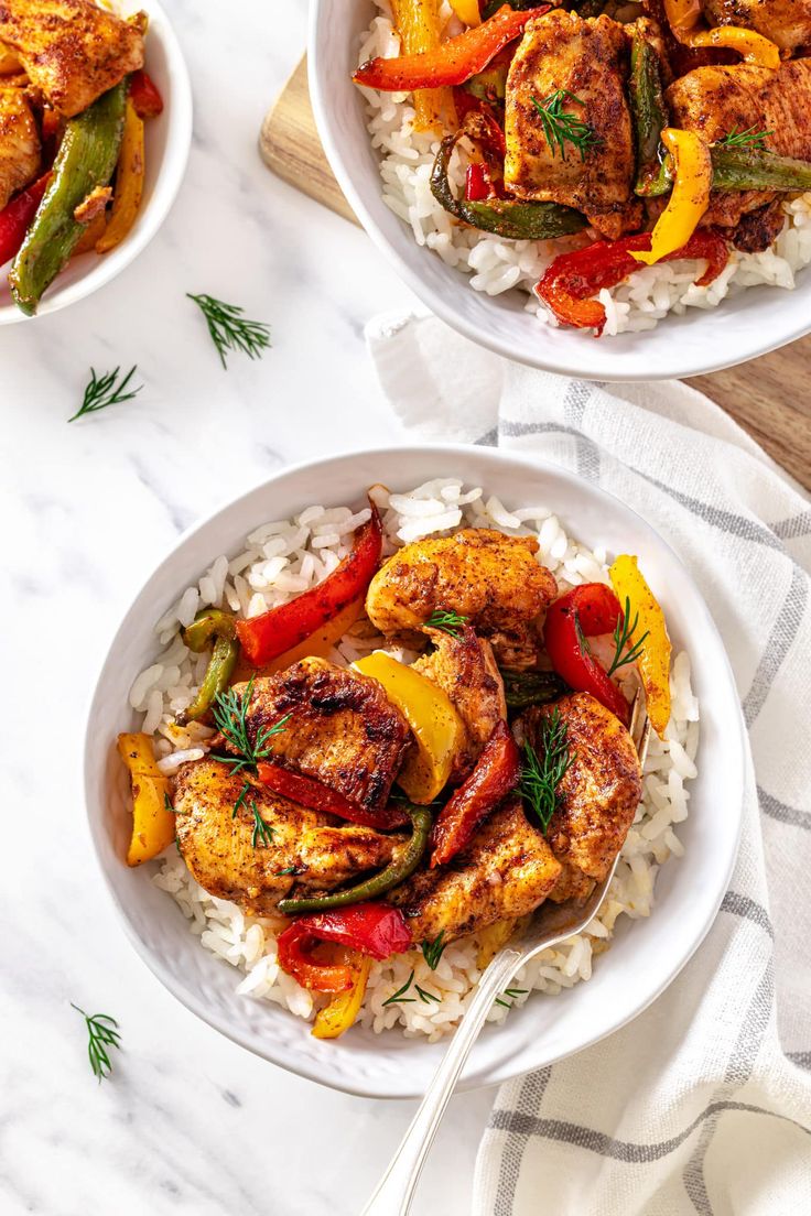 two white bowls filled with chicken, peppers and rice