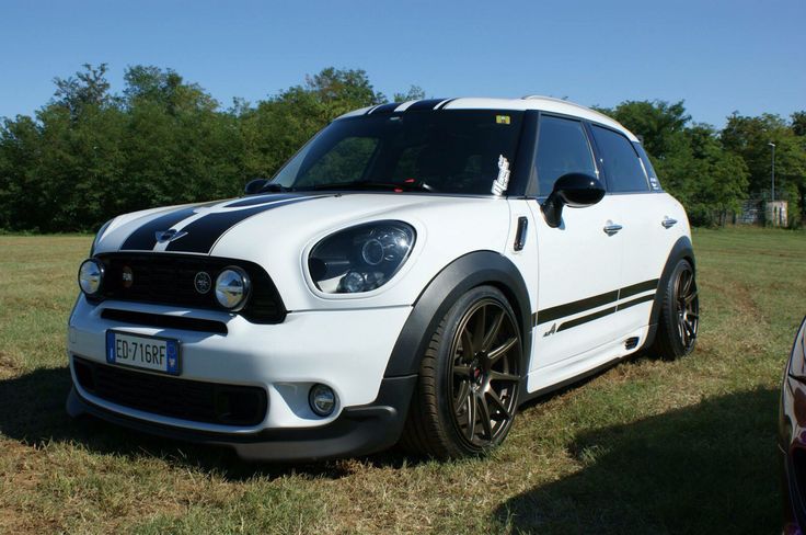 a small white car parked on top of a grass covered field with trees in the background