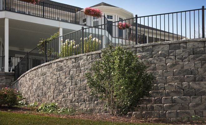 a stone wall and fence in front of a house with flowers growing on the balconies