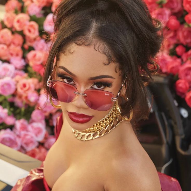 a woman wearing red sunglasses and gold chains around her neck with flowers in the background