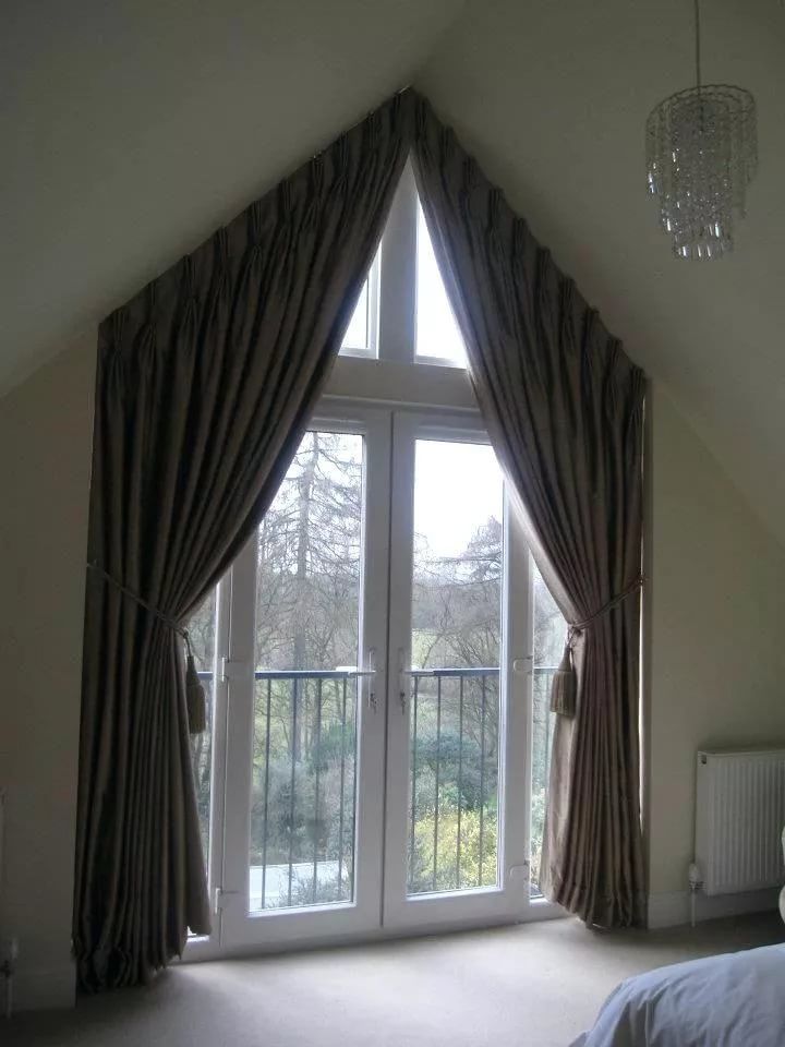 a bedroom with a large window and curtains on the windowsill, along with a chandelier hanging from the ceiling