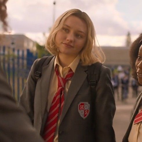 two women in school uniforms standing next to each other on the street, one wearing a red and white striped tie