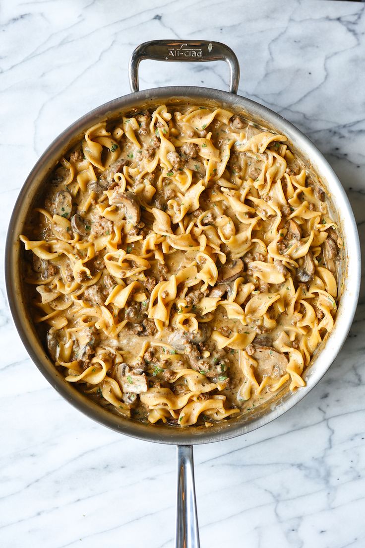 a pot filled with pasta and meat on top of a marble countertop next to a spatula