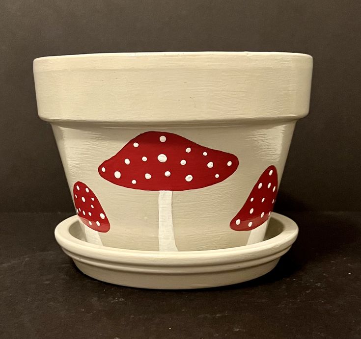 a white bowl with red mushrooms painted on the front and bottom, sitting on a black surface