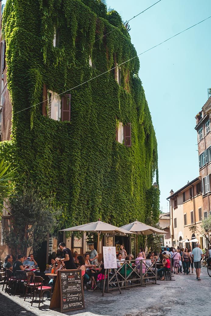 people are sitting at tables in front of a building covered with green plants and vines