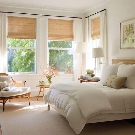 a white bed sitting in a bedroom next to two windows with shades on them and an arm chair