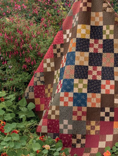 a patchwork quilt hanging from a tree in a field full of wildflowers