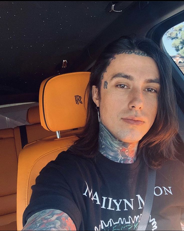 a man with long hair and tattoos sitting in the back seat of a car looking at the camera