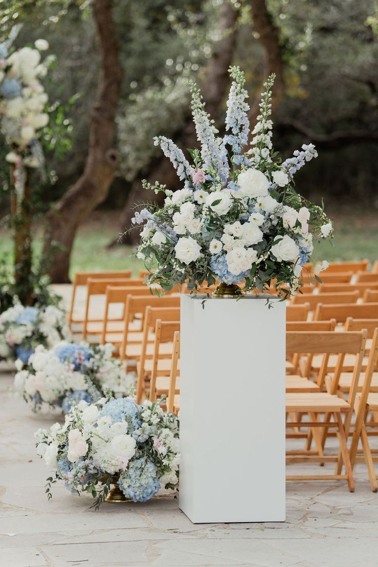 an outdoor wedding ceremony with white and blue flowers in vases on the side of the aisle