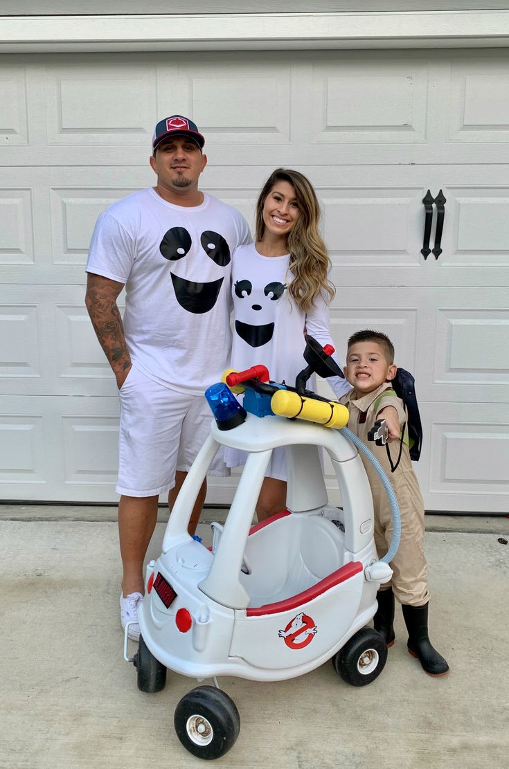 a man and woman standing next to a child in front of a garage with a toy car