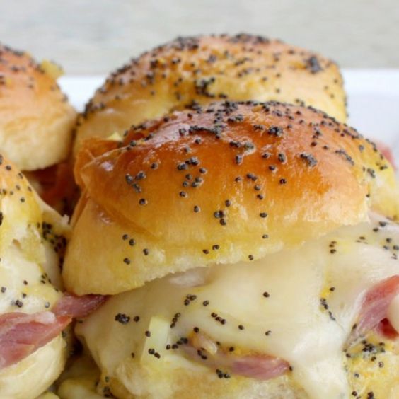 ham and cheese sliders with melted cheese on them sitting in a white paper container