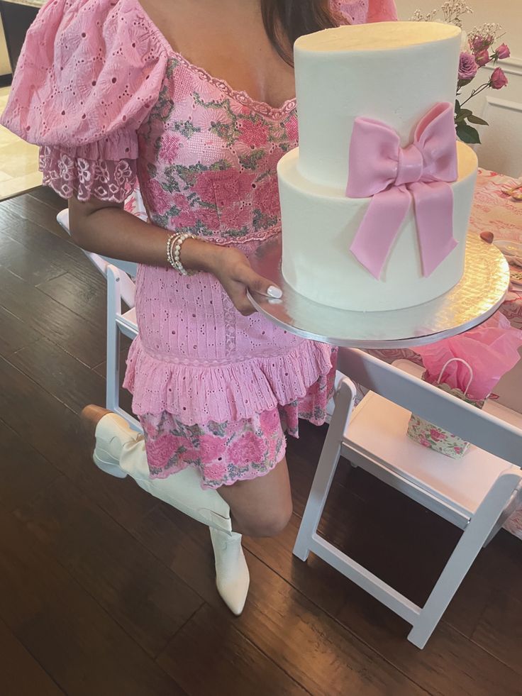 a woman holding a large white and pink cake