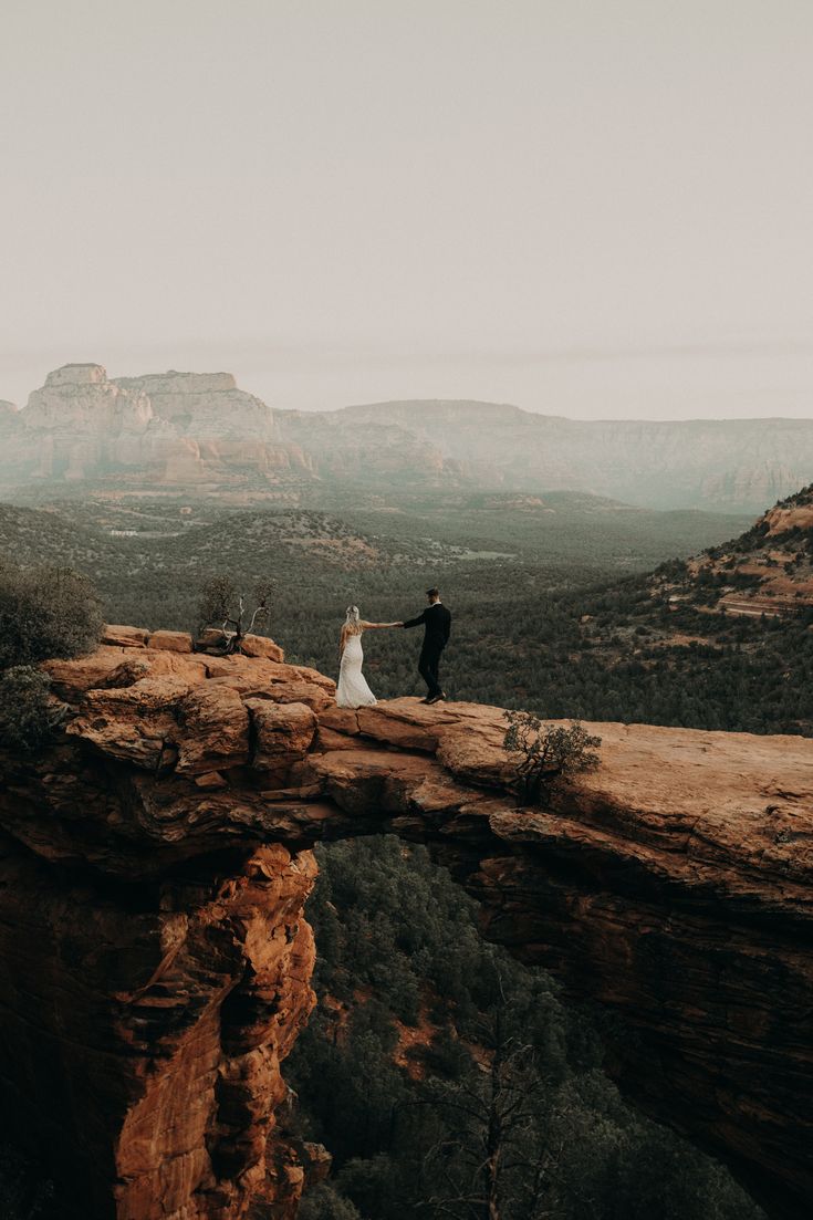 a bride and groom standing on top of a cliff