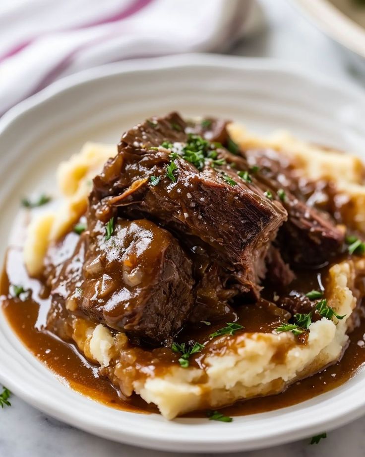 a white plate topped with mashed potatoes and beef on top of gravy