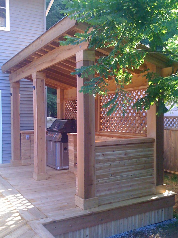 a wooden gazebo sitting on top of a wooden deck next to a building with a grill