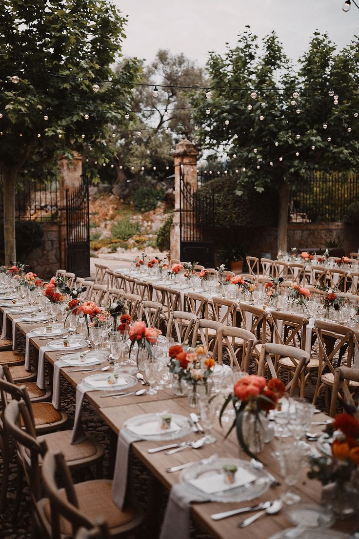 a long table set up with place settings and flowers on it for an outdoor wedding