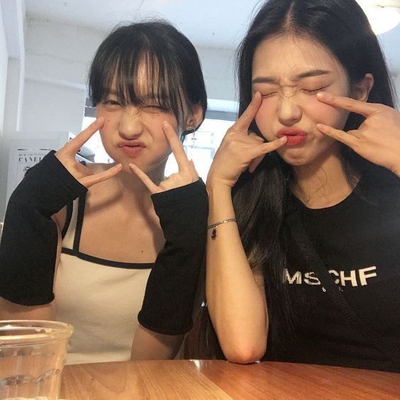 two young women sitting at a table with their hands in the air while making faces