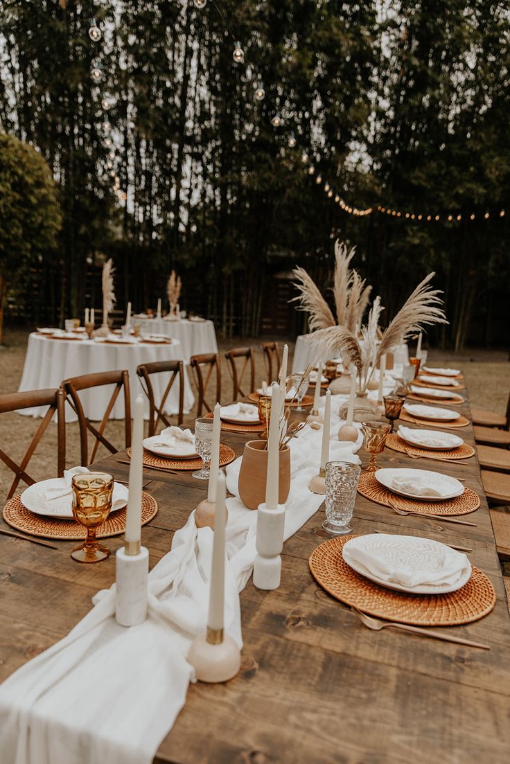 a long table with white linens and place settings is set for an outdoor dinner