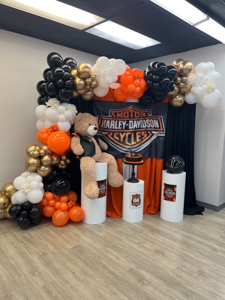 an orange and black balloon arch with a teddy bear