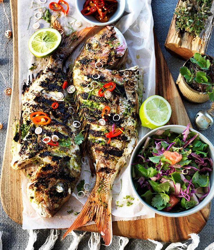 two fish are on a cutting board next to some salads and dipping sauces