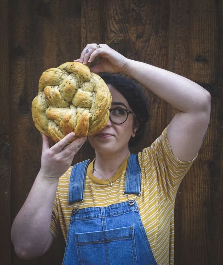 a woman holding up a loaf of bread in front of her face and covering it with her hands