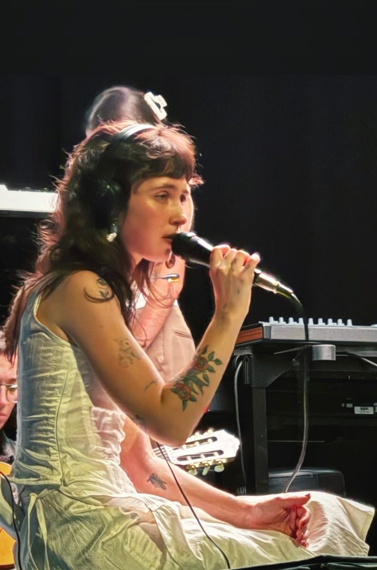 a woman with headphones on sitting in front of a piano and singing into a microphone