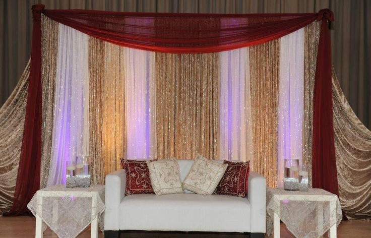 a white couch sitting in front of a red and gold curtained wall with candles on it