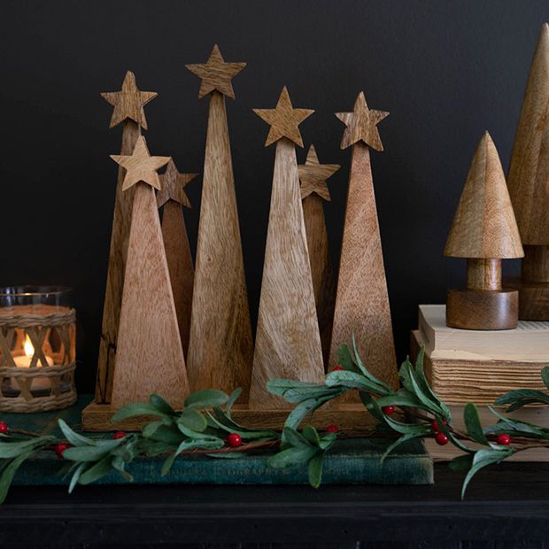 wooden christmas trees are lined up on a mantle next to a candle and some books