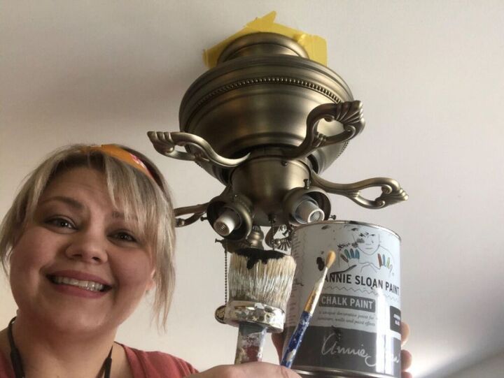 a woman is holding a paintbrush and a can in front of a ceiling fan