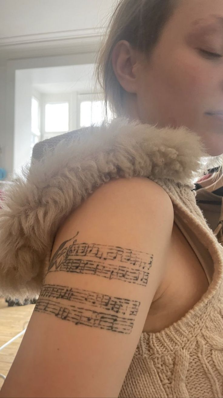 a woman with a tattoo on her arm is looking down at the music sheet she has written on