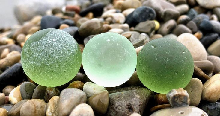 two green and white balls sitting on top of some rocks next to eachother