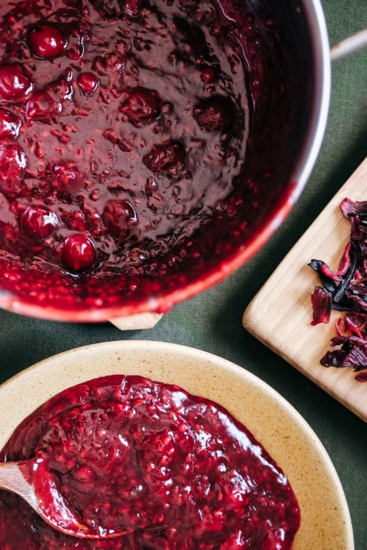 two bowls filled with cranberry sauce next to a cutting board and wooden spoon