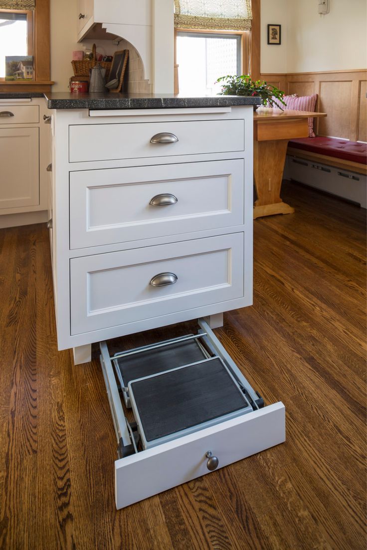 an open drawer in the middle of a kitchen with wood flooring and white cabinets